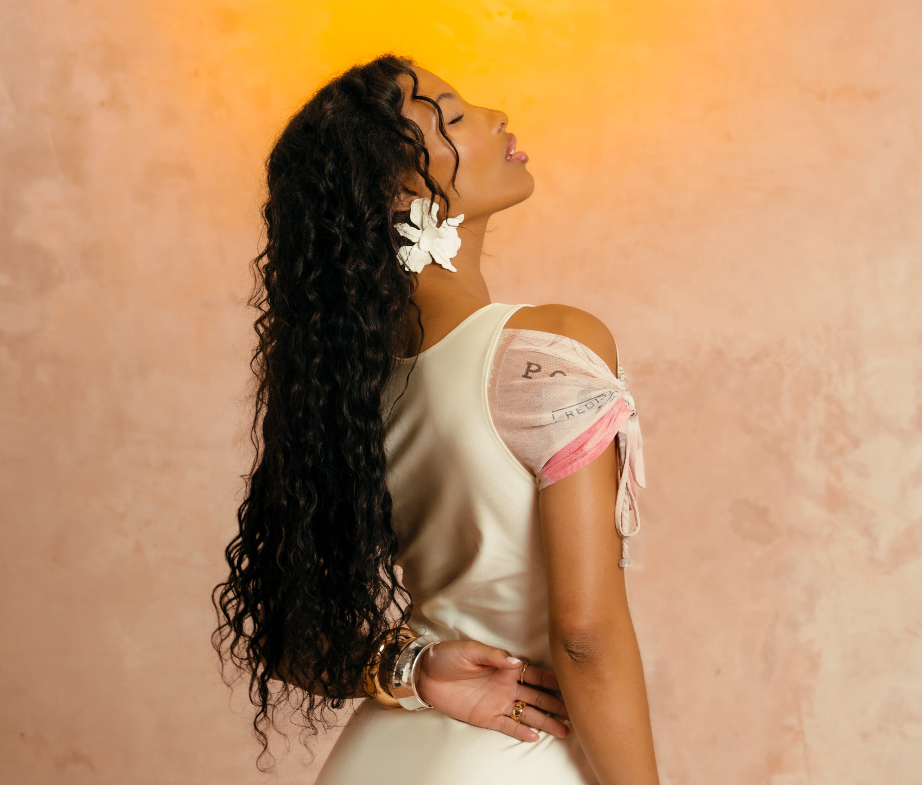 Woman in a white dress with sheer sleeves against a warm-toned wall